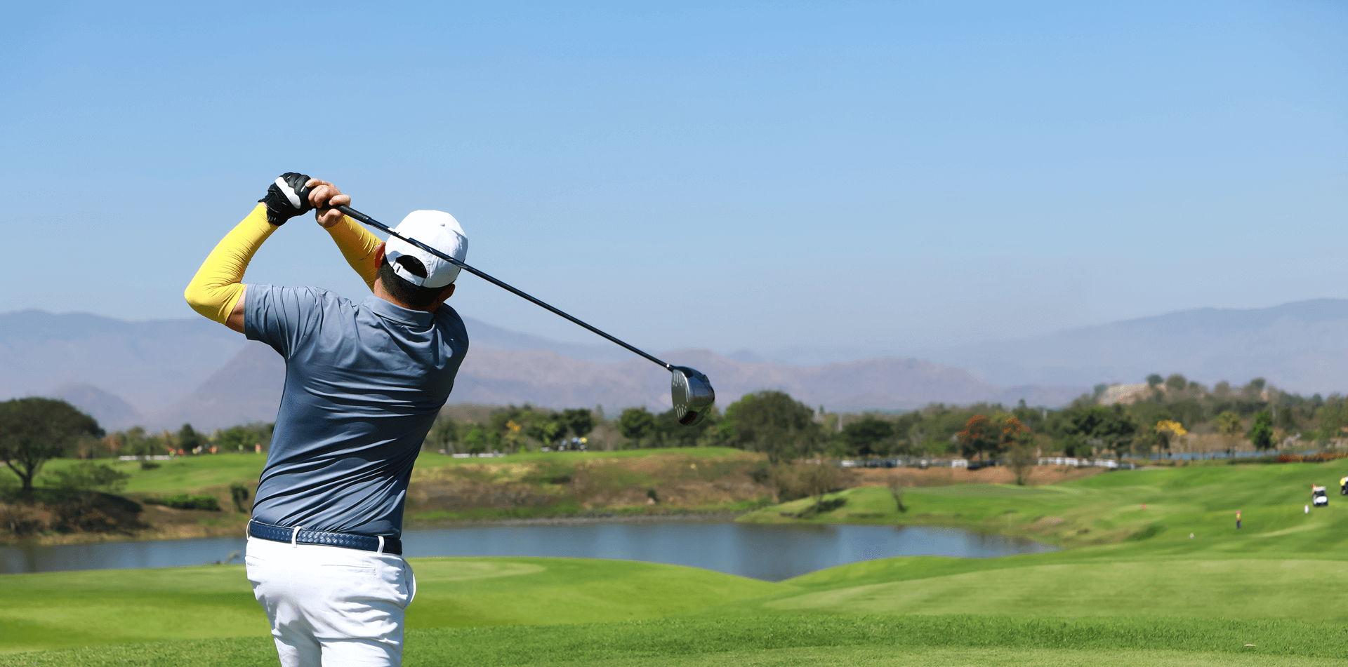 home-hero Male golfer after hitting a golf ball overlooking a pond and hills